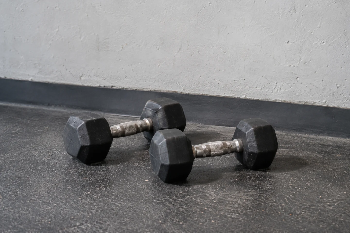Two modest-weight hex dumbbells beside a plain gym wall.