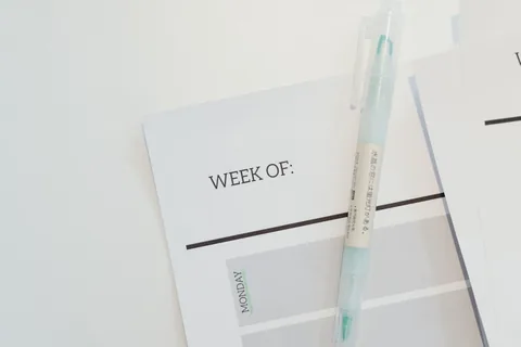 A weekly paper planner and pen on a desk.