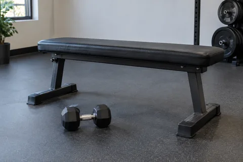 Flat weight bench with one light dumbbell placed beside it.